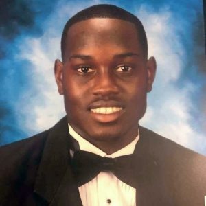 Color photo of Ahmaud Arbery, a young black man wearing a tuxedo and smiling.