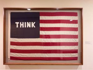 Photo of a framed US flag, except that instead of white stars on a blue field, the upper left area of the flag contains the word THINK in white all-caps on a blue field.