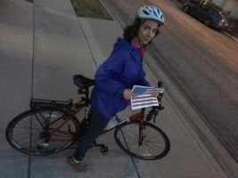 Photograph of me on my bike, wearing a bike helmet and carrying a small paper printout of a US flag