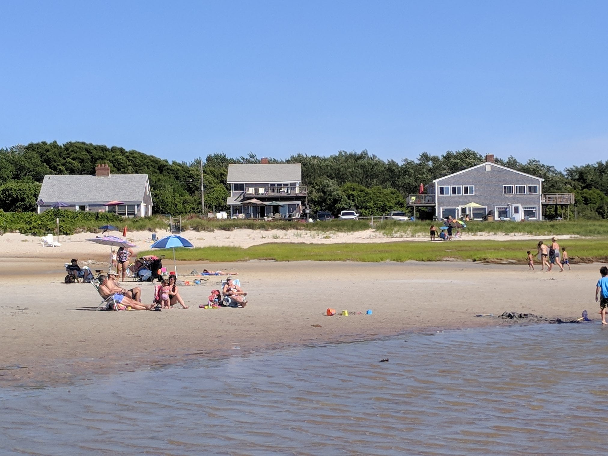 Photo of three houses built right up next to a sandy beach with water in the foreground