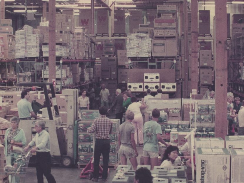 Vintage photo of people shopping among stacked-up racks of merchandise at an early Costco