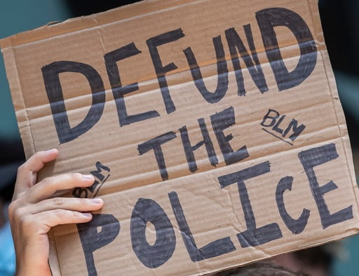 Cardboard sign with handwritten words "DEFUND THE POLICE BLM"