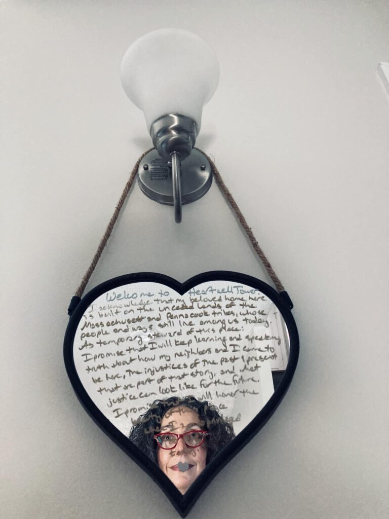 Photo of a heart-shaped mirror hanging from a wall sconce. I have written a message on the mirror in metallic pen. My face is reflected behind the writing. My handwriting is terrible; the article includes the handwritten text so it's readable. 