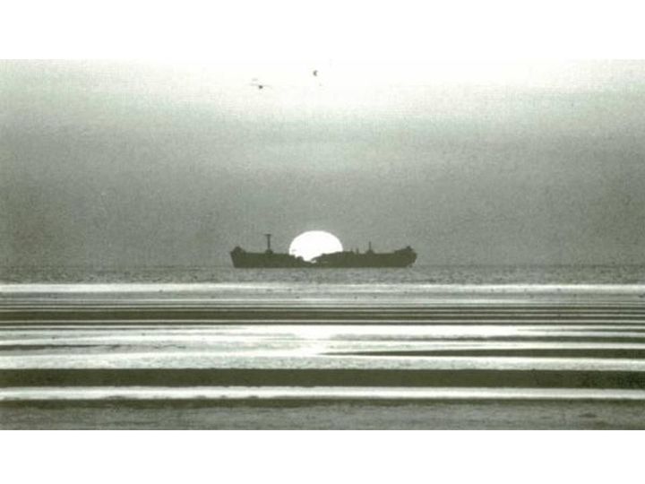 Old black and white photo of the wreck of the SS James Longstreet with the sun setting behind it and tidal flats in the foreground