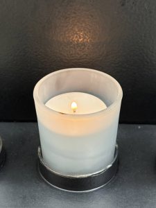 A votive candle burns with a small flame in a frosted glass candle-holder.