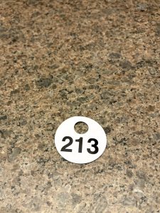 A small white disc with the number "213" on it in black, with a hole in the disc as though for a chain. It's lying on a tan-patterned granite countertop.
