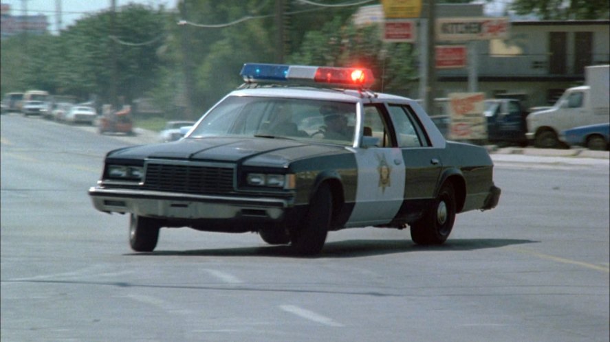 Stock image of a 1980s-era police car making a sharp turn in the middle of a city street