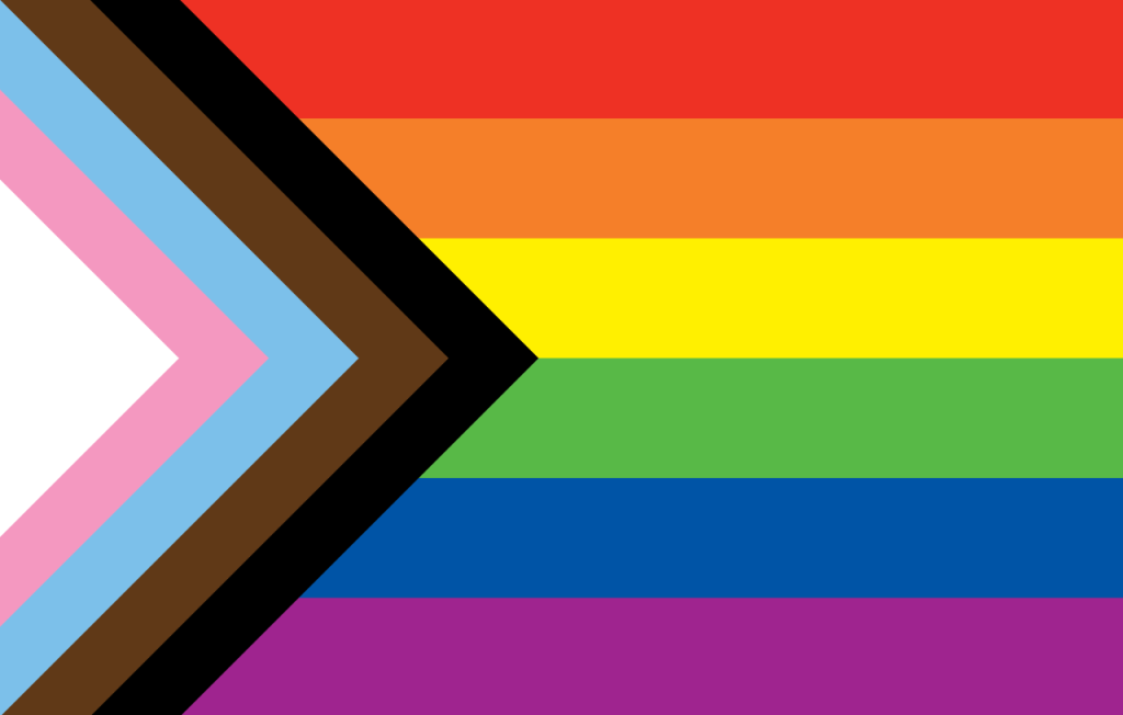 The Progress Pride flag, featuring horizontal rainbow stripes with triangular white, pink, light blue, brown, and black stripes at left. 