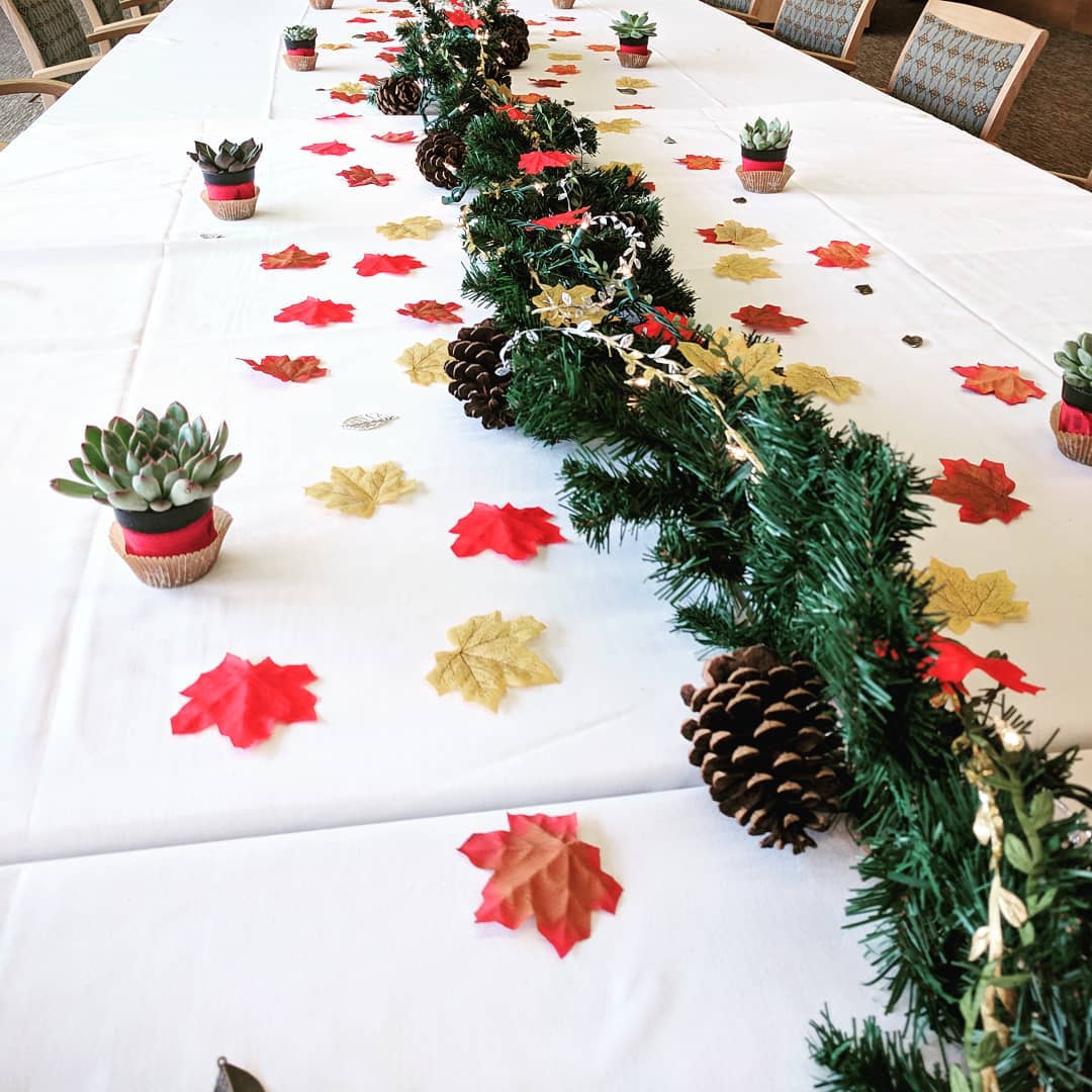 long dining table with pine garland and leaves scattered along it with twinkle lights