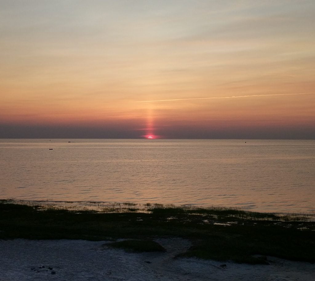 Sun setting into the ocean with a beam of light coming up from the sun