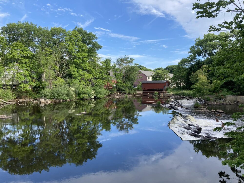 A mirror-smooth river falls over a dam, reflecting trees and sky.