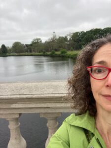 A selfie of half my face, with a view behind me of a bridge railing and a river beyond that.